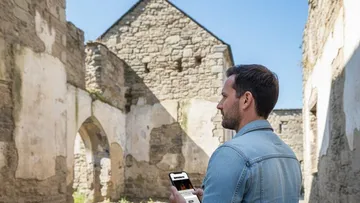 Man holding smartphone in stone ruins.