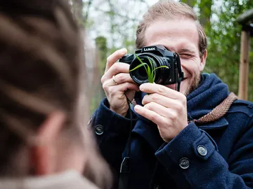 Mann hält Kamera, lächelt und fotografiert im Freien.