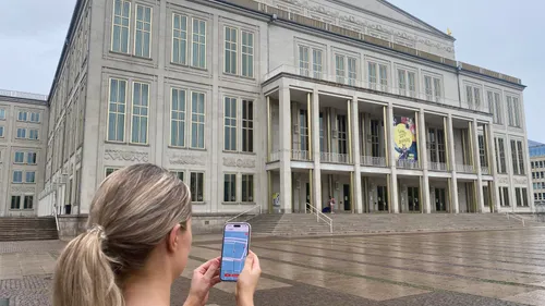 Person fotografiert großes Gebäude mit Smartphone draußen.