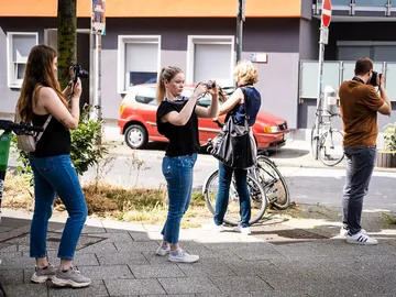 Vier Personen fotografieren auf einer Stadtstraße an einem sonnigen Tag.