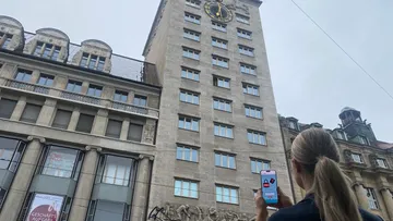 Person hält Handy vor hohem Gebäude.