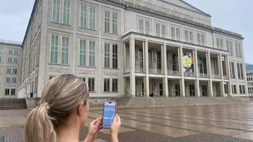 Person nutzt Handy vor Theatergebäude.