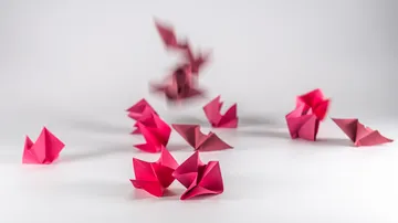 Red origami boats scattered on white surface.