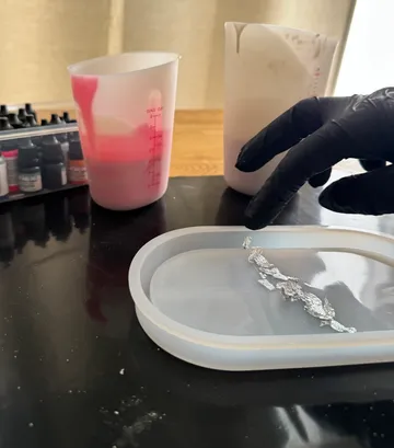 Behandschuhte Hand fügt Folie zur Silikonform hinzu.