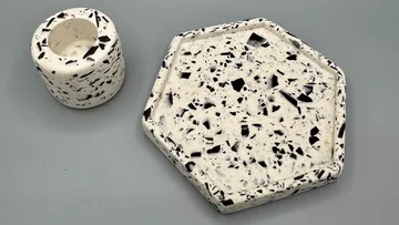 Terrazzo-Untersetzer und Pflanzgefäß auf grauer Fläche.