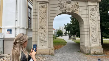 Frau fotografiert verzierte Steintoranlage im Freien.