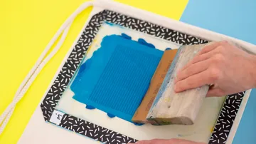 Hände drucken blaue Tinte auf Rahmen.