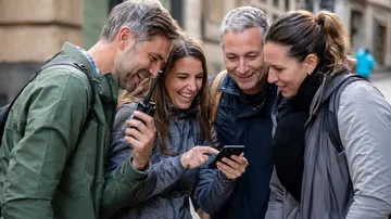 Gruppe von Menschen schaut draußen auf ein Handy.