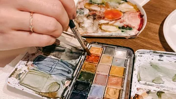 Hand malt mit Aquarellfarben auf Tisch.