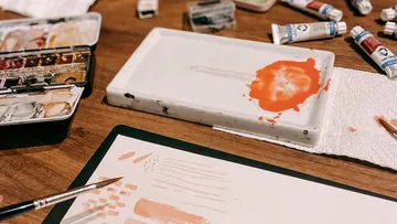 Pinsel malen auf Papier, umgeben von Farben.