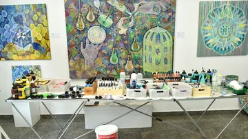 Art supplies on table, colorful paintings displayed.