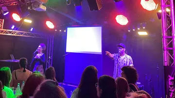 Zwei Künstler auf Bühne unter bunten Lichtern.