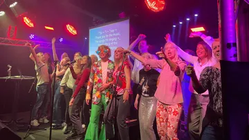 Group singing karaoke on stage with lights.