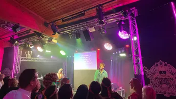 Person singing onstage with colorful lights.