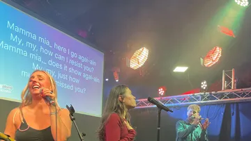 Three people singing on a lit stage.