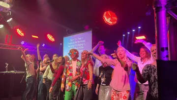 Gruppe singt auf der Bühne mit bunten Lichtern.