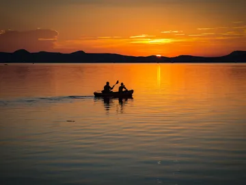 Zwei Menschen kajaken bei Sonnenuntergang auf ruhigem Wasser.