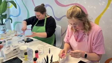 Zwei Frauen basteln mit Farben am Tisch.