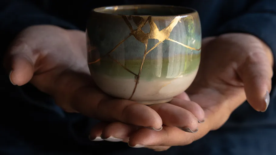 Hands holding a repaired pottery cup.