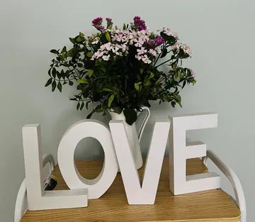 Blumen im Krug neben "LOVE" Buchstaben auf Tisch.