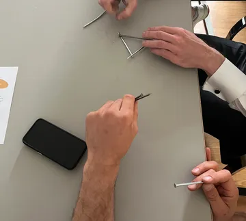 Hands holding nails on a table.
