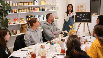 Woman teaching calligraphy to seated group inside shop.