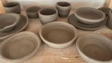 Clay bowls drying on wooden shelf.