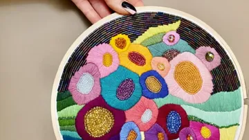Hand holding colorful embroidered hoop art.