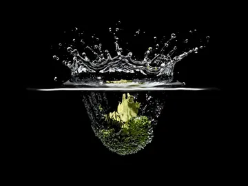 Brokkoli taucht ins Wasser, erzeugt Spritzer, schwarzer Hintergrund.