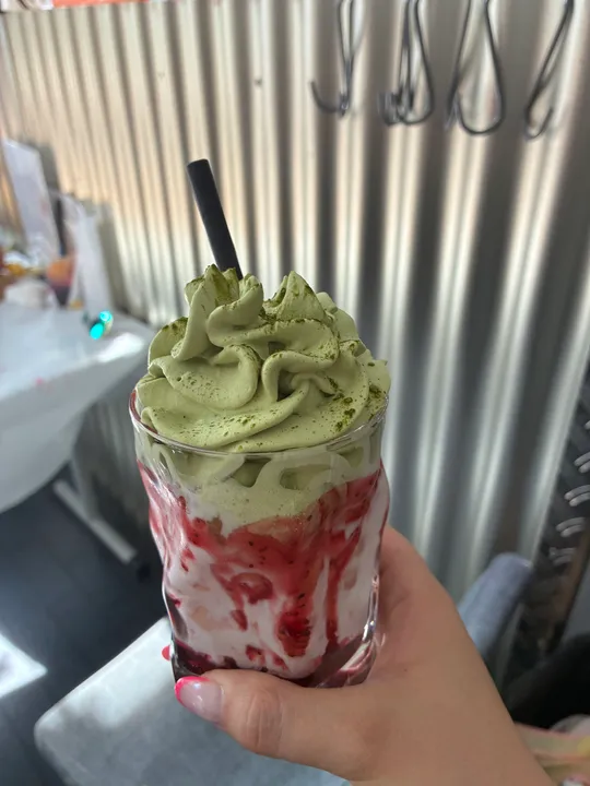 Hand hält Matcha-Getränk mit Strohhalm im Café.