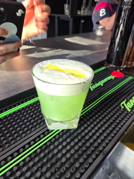 Grüner Cocktail mit Schaum auf Barmatte.