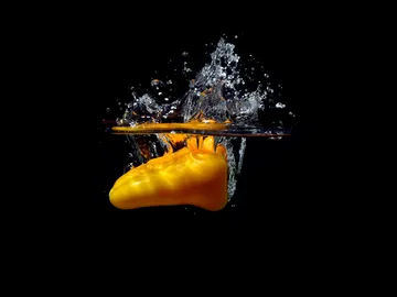 Gelbe Paprika taucht in Wasser und erzeugt Spritzer.