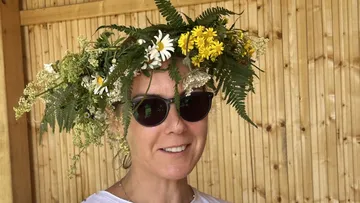 Frau mit Blumenkronen lächelt im Holzraum.