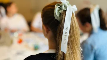 Woman with ribbon reading 'TEAM BRAUT' in hair.