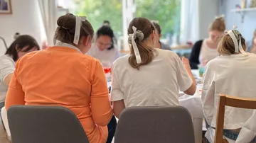Women crafting at table in bright room.