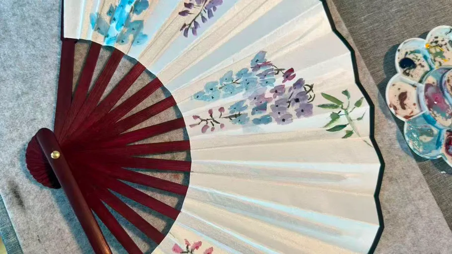 Decorative fan with floral painting, lying on table.