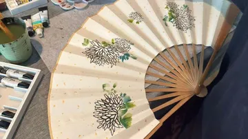 Decorative fan on table with painting supplies.