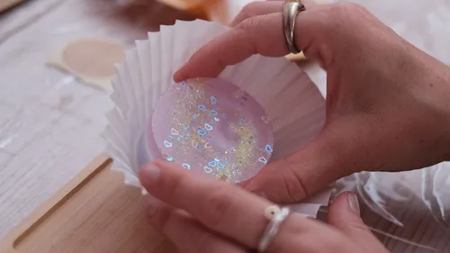 Hands holding a purple glittery sphere.