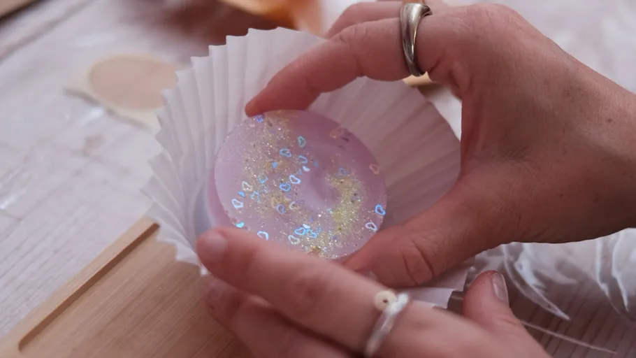 Hände halten eine glitzernde lila Kugel.