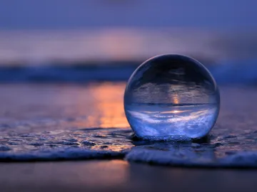 Glaskugel reflektiert Sonnenuntergang am Ufer. Sand und Wasser.