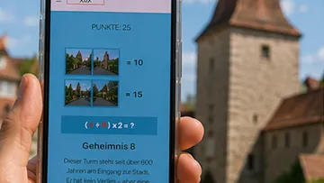 Hand holding phone displaying puzzle, tower in background.