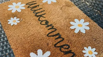 Welcome mat with daisies on wicker surface.