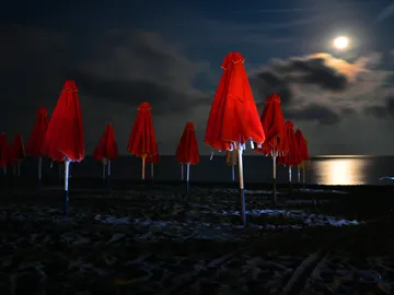Red umbrellas are placed on the beach under bright moonlight.