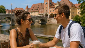 Paar sitzt lächelnd am Fluss, Brücke dahinter.