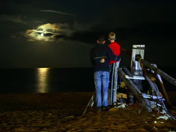 Vater und Sohn betrachten den Mond über dem Meer.