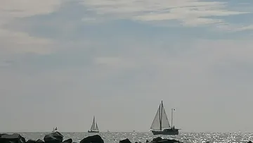 Segelboote segeln auf ruhiger See unter Wolkenhimmel.
