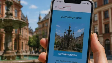 Hand holding phone displaying Kochbrunnen image.