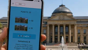 Handy zeigt Rätsel-App vor historischem Gebäude.