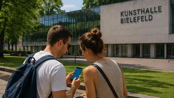 Zwei Personen schauen auf Handy vor Kunstmuseum.