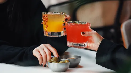 Zwei Hände stoßen mit Gläsern über Tisch an.